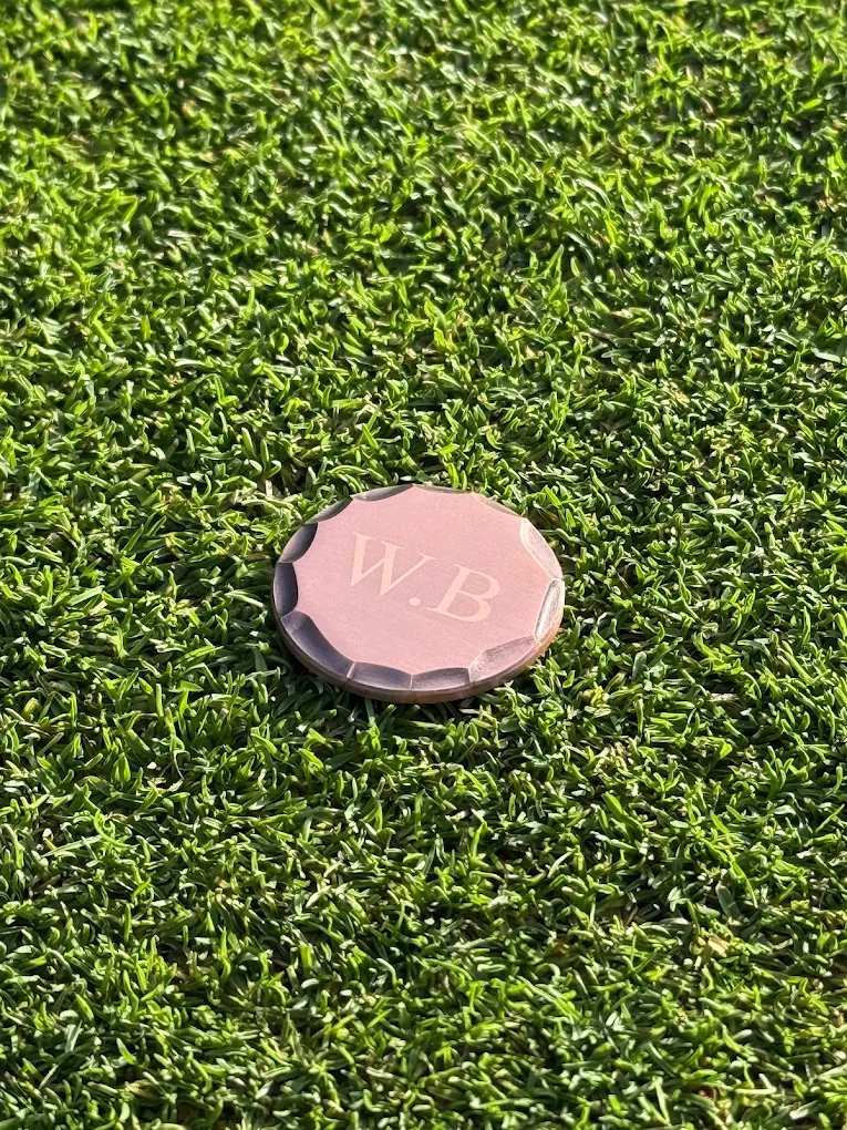 Copper ball marker with W.B initials on golf green grass